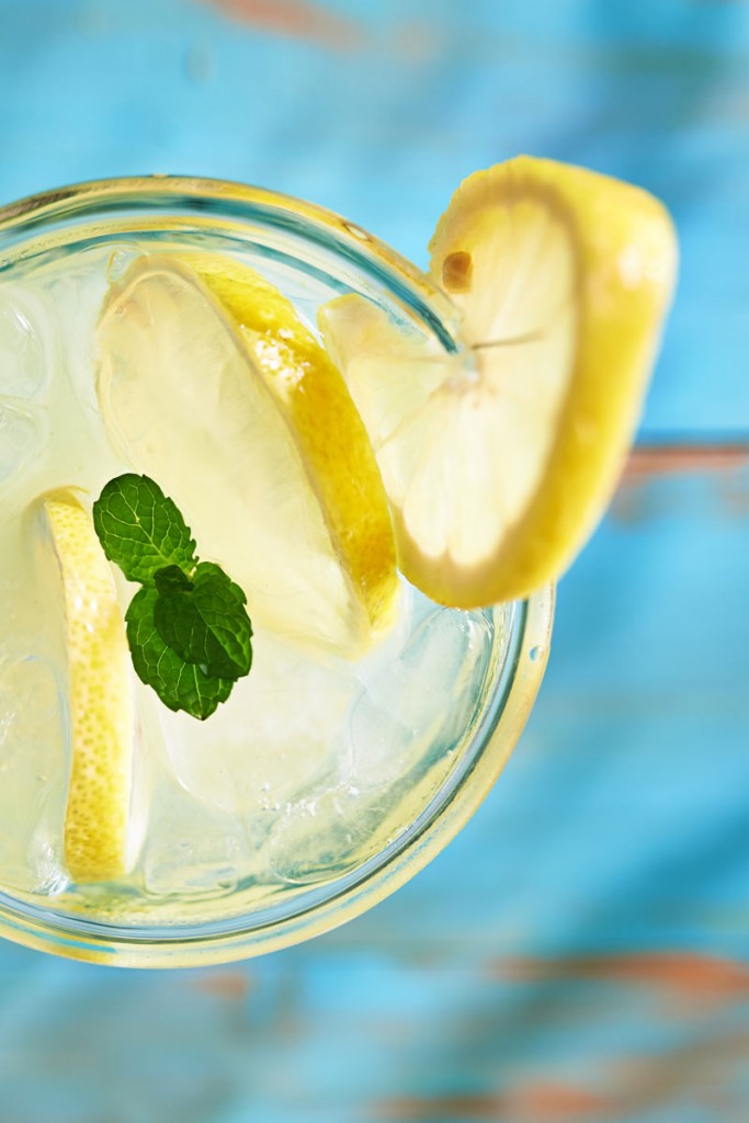 A fresh drink close up with a slice of lemon and mint leaf on top