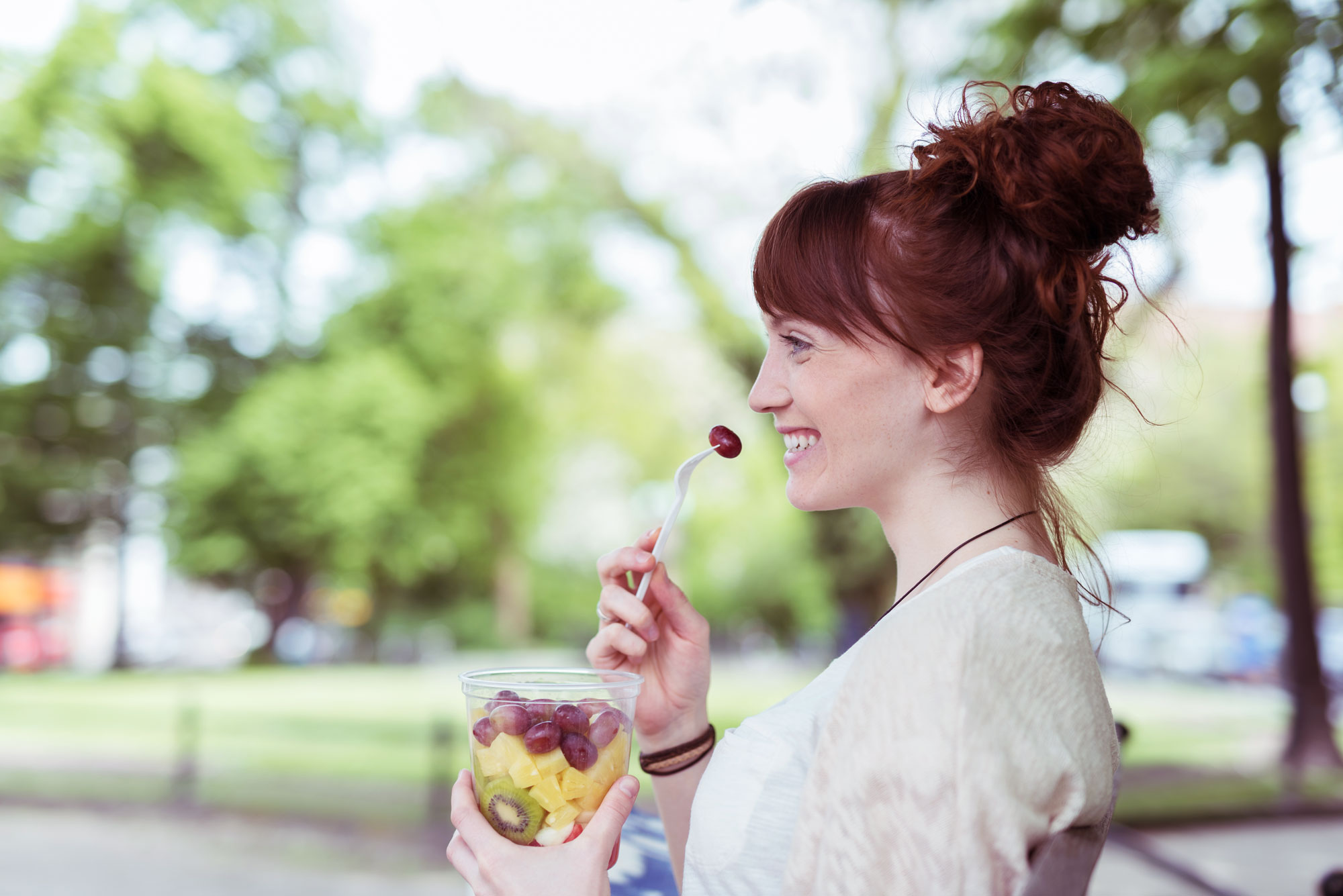 A happy woman enjoying a cup of fruit in park background