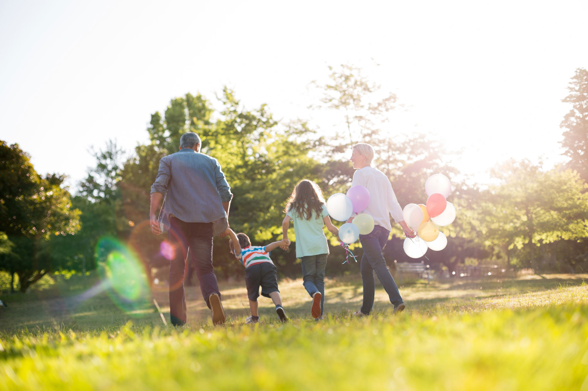 A happy family's appearance from behind with variety colour of balloons in a sunny weather at the park