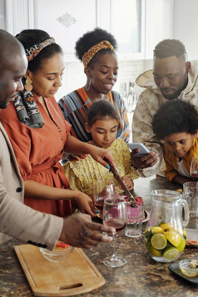 a family standing around the kitchen counter making a pitcher water with fresh citrus fruit